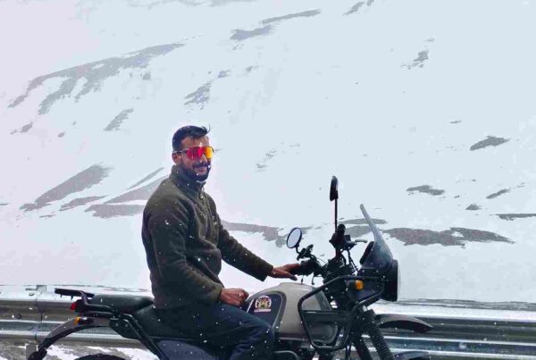 Group of bikers on the Delhi to Ladakh bike trip riding through Himalayan roads toward Leh with prayer flags and rugged landscapes
