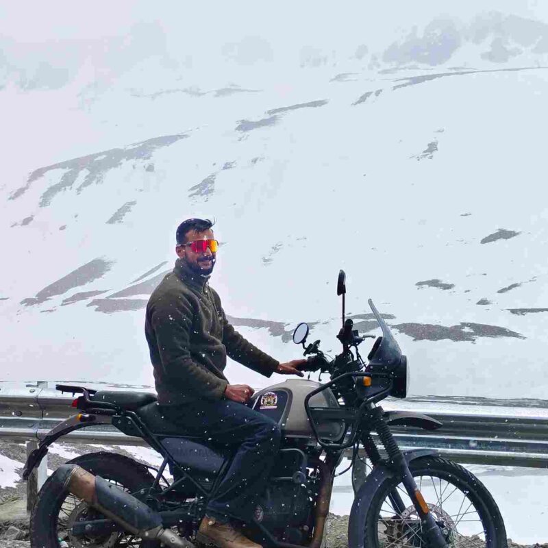 Group of bikers on the Delhi to Ladakh bike trip riding through Himalayan roads toward Leh with prayer flags and rugged landscapes
