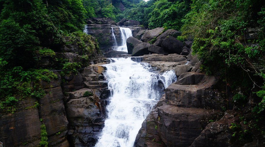 Mist-covered Bophill Falls near Dawki surrounded by dense greenery