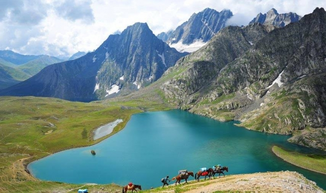 Crystal-clear Tarsar Lake surrounded by green meadows and clouds