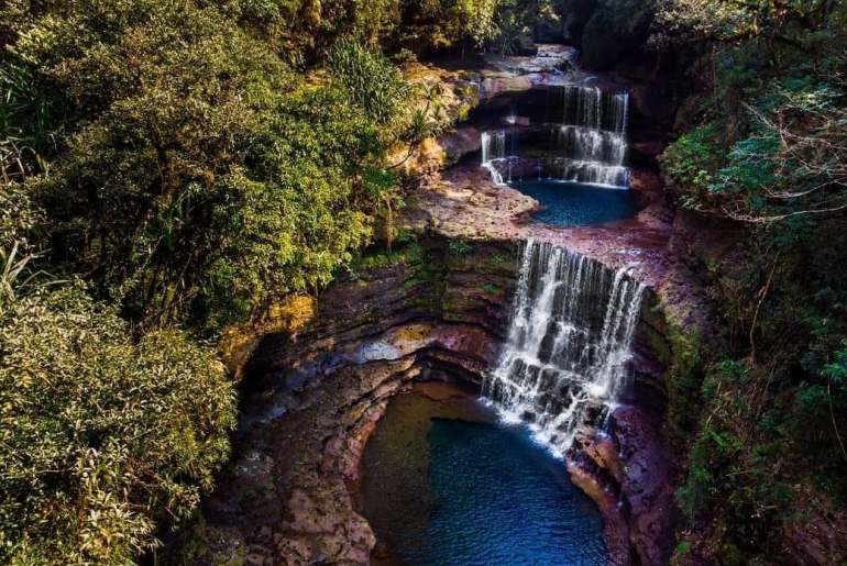 Three-tiered Wei Sawdong Falls surrounded by forest and rocks